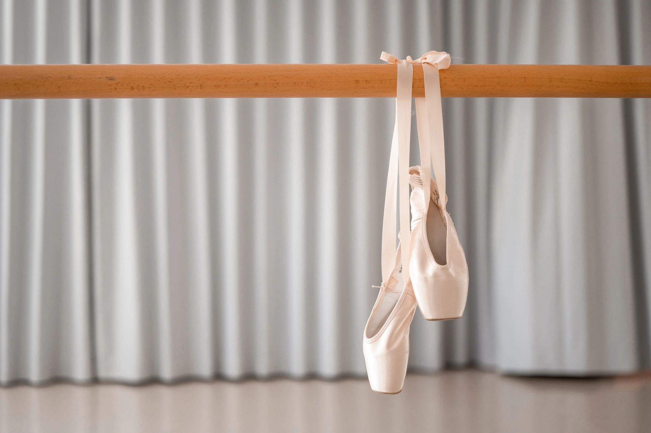 Pair of pink ballet shoes hanging on a barre in a studio